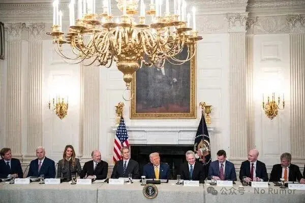 A line of people sit at a long table under a large chandelier, with President Trump at the center and Mr. Sacks to his right.